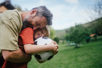 Dad having fun with young son, playing football, running and catching each other. Playing on a lawn...