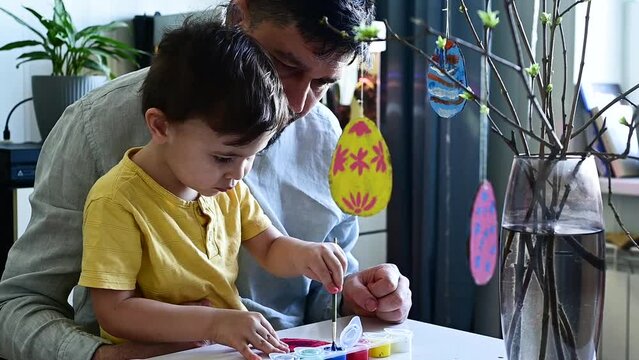 Dad and son paint cardboard eggs for Easter