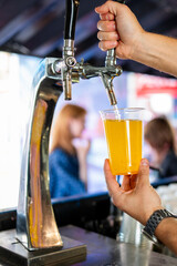 Hand pouring lemonade from a tap into a clear glass with blurred background