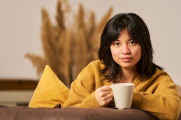 A woman in a yellow sweater is holding a white coffee cup