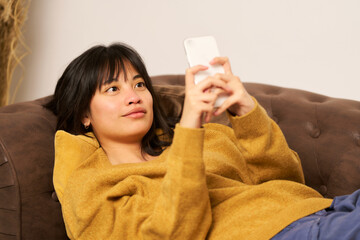A woman is laying on a couch and looking at her phone