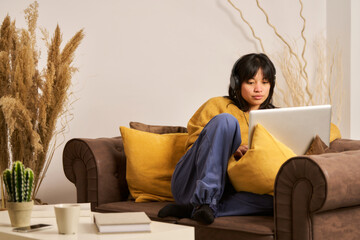 A woman is sitting on a couch with a laptop in front of her