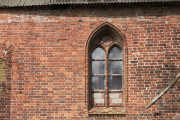 A beautiful Gothic lancet window in the wall of an old church. Traces of sloppy modern repairs are visible. Plastic glass is installed in the frames. Background.