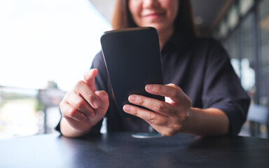 Closeup image of a young woman holding and using mobile phone in cafe
