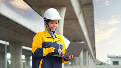 Asian female engineer uses laptop to inspect highway construction work
