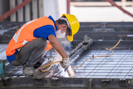 Construction worker engaged in welding work. He is crouching down on a metal framework welding, visible sparks and light emanating from the welding torch is Building construction business concept.