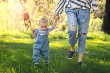 baby's first steps, mother and one-year-old child walk on the grass