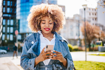 Beautiful black woman walks down the street and uses smart phone for chat messaging and...
