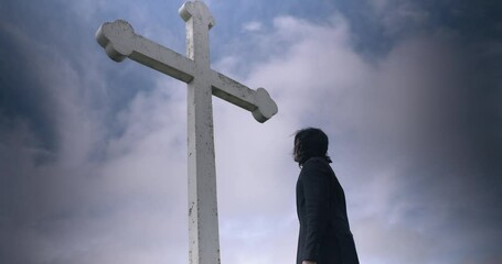 Religious, prayerful man praying and worshipping in front of white Christian cross monument.