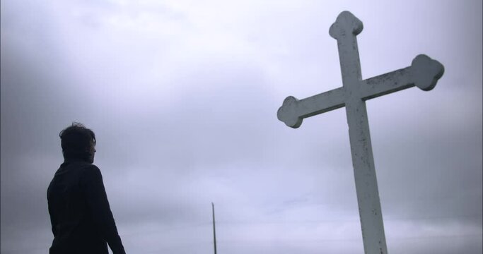 Young, religious man in black suit worshipping and praying in front of Christian cross.