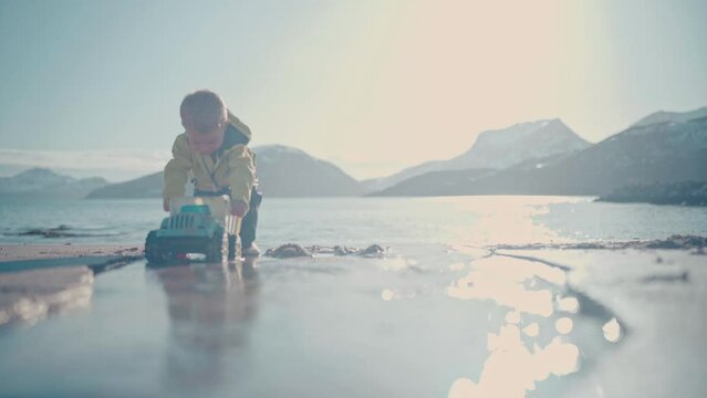 Boy plays with toy dump truck on a beautiful beach in Northern Norway right outside of Tromso, Norway. With big mountains in the background, this is a stunning capture. #untraceableglobal