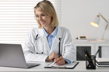 Smiling doctor with laptop having online consultation at table in office