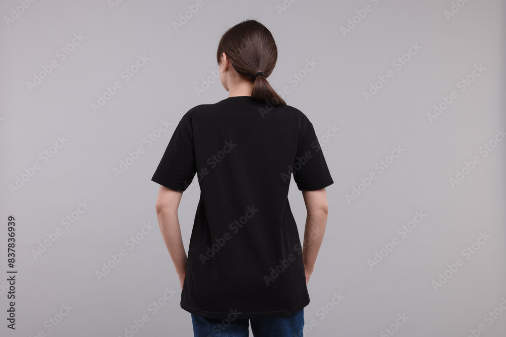 Wall mural Woman in stylish black t-shirt light grey on background, back view - Wall murals
