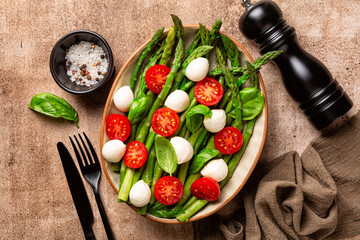Top view of asparagus salad, asparagus, tomatoes, mozzarella cheese, basil leaves on a brown table background.