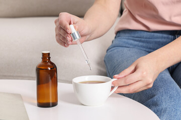 Woman dripping food supplement into cup at white table indoors, closeup