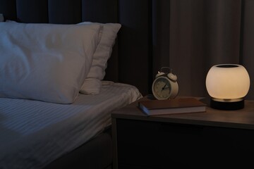 Nightlight, alarm clock and book on bedside table near bed indoors