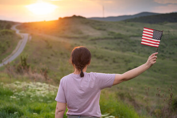 Woma holding a waving american USA flag outdoor in the sunset.