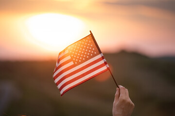 Woman`s hand holding a waving american USA flag in magic sunset.