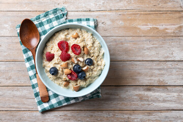 Oatmeal porridge with raspberries, blueberries and almonds in bowl on wooden table. Top view. Copy...