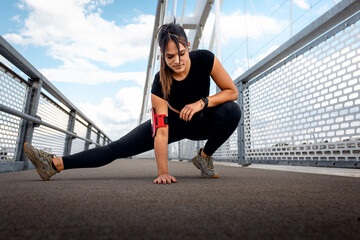 Young fitness woman in black sport outfit preparing for a run stretching her muscles at bridge.