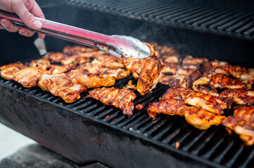 Close-up of marinated chicken meat grilling with smoke rising.