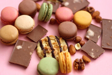 Pastel macarons, almond chocolate, peanut butter cookies and various nuts on bright pink background. Selective focus.