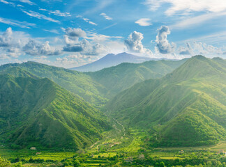 Fototapeta premium amazing view at a green landscape between two mountains with a high peak with snow and blue cloudy sky on background