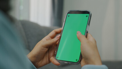 A woman uses a mobile phone or tablet with a green screen to watch videos, surf social media, or have an online conference.