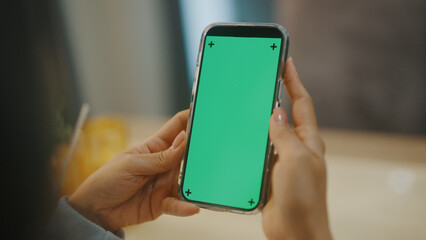 A woman uses a mobile phone or tablet with a green screen to watch videos, surf social media, or have an online conference.