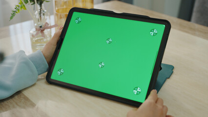 A woman uses a mobile phone or tablet with a green screen to watch videos, surf social media, or have an online conference.