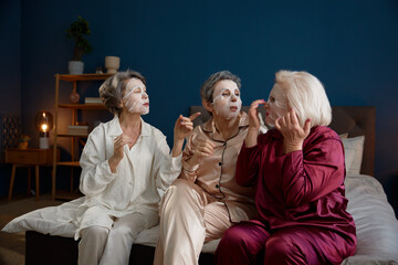 Senior women applying anti-aging cotton facial mask having fun together