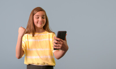 A girl is holding a cell phone and smiling. The girl is happy and excited about something on her phone