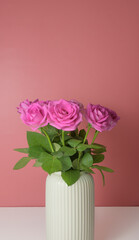 A vase of pink roses sits on a table on pink background