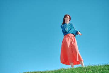 Teen girl standing on green grass against clear blue sky, covering nose with hand and showing...