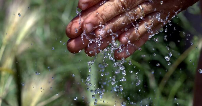Super slow motion macro of young man is washing hands with clear pure water flowing stream and splashing drops on green nature background at 1000 fps. Personal care and hygiene natural products.