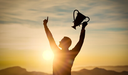 Success, joint achievement of goal in business and life. Winning is holding trophy in hand. Silhouette of man hand with trophy in sunset