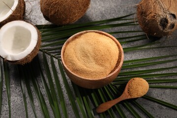 Coconut sugar in bowl, spoon, palm leaves and fruits on dark textured table, closeup