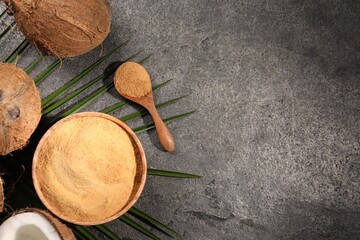 Coconut sugar in bowl, spoon, palm leaves and fruits on dark textured table, flat lay. Space for text