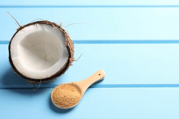 Spoon with coconut sugar and half of fruit on light blue wooden table, closeup. Space for text