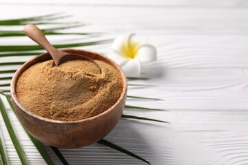 Coconut sugar and spoon in bowl on white wooden table, closeup. Space for text