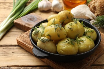 Tasty young boiled potatoes with dill in bowl on wooden table