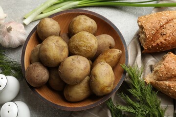 Tasty young boiled potatoes in bowl served on grey table, flat lay