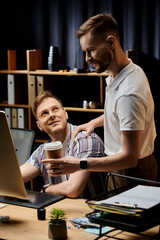 Two loving men in business attire seated at desk with cup of coffee.