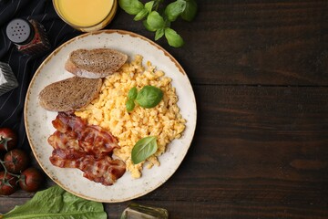 Delicious scrambled eggs with bacon and products on wooden table, flat lay. Space for text