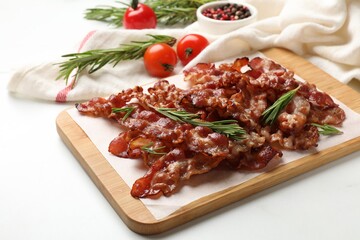 Slices of tasty fried bacon with rosemary on white table