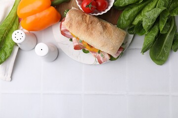 Tasty sandwich with bacon, tomatoes, greens and bell pepper on white tiled table, flat lay. Space for text