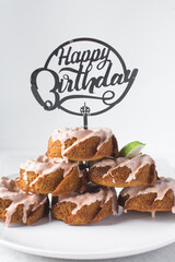 Happy birthday sign on a stack of iced mini bundt cakes, individual birthday cakes, bundtlettes stacked with a happy birthday cake topper