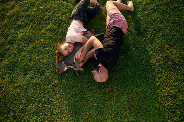 Top view, lying on the grass. Man and woman are with dog on the field