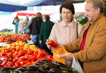 Mature married couple in casual clothes choosing organic bell peppers during date at local grocery...