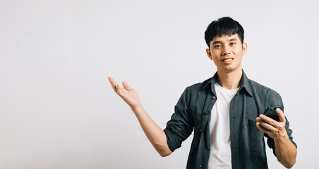 Portrait Asian smiling young man holding mobile phone and hand open to empty space studio shot...